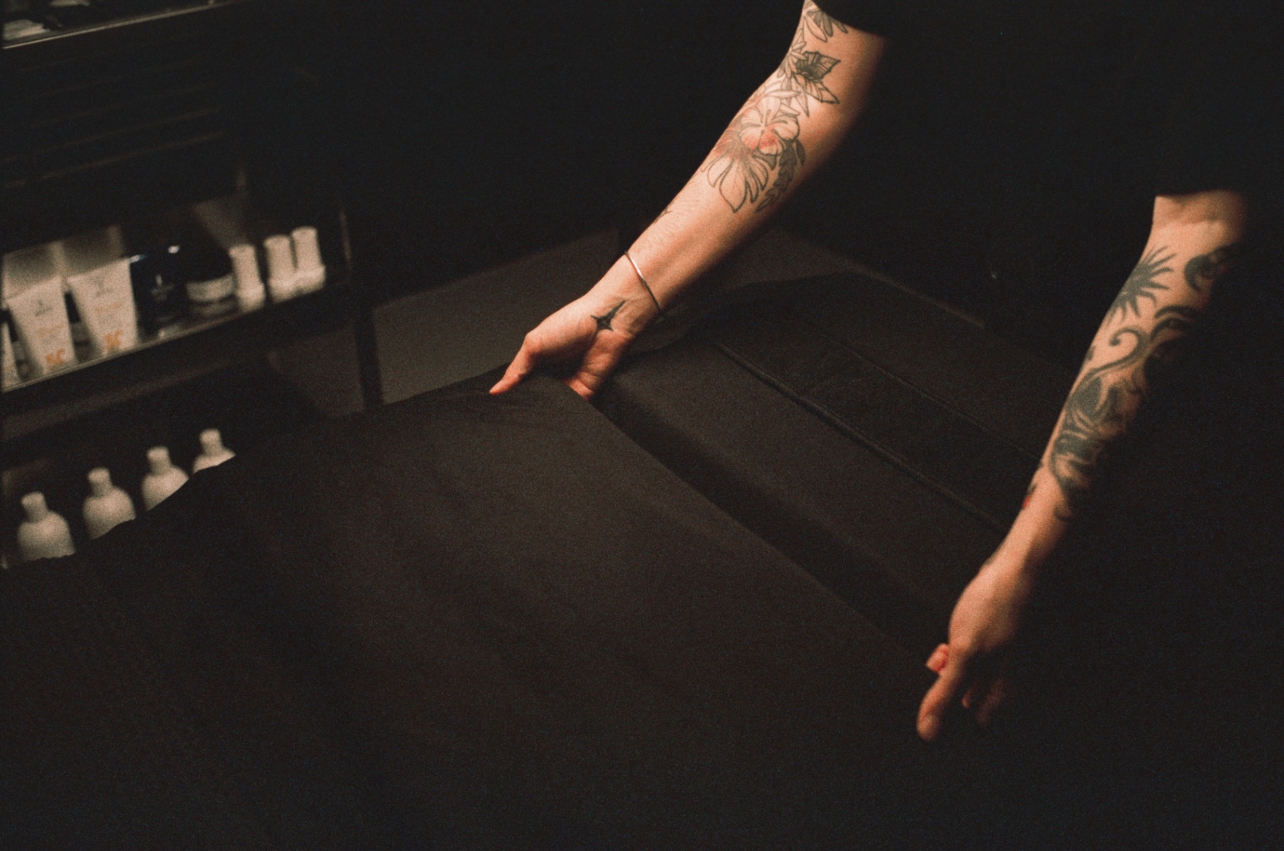 Tattooed hands smoothing the sheet on a black treatment bed